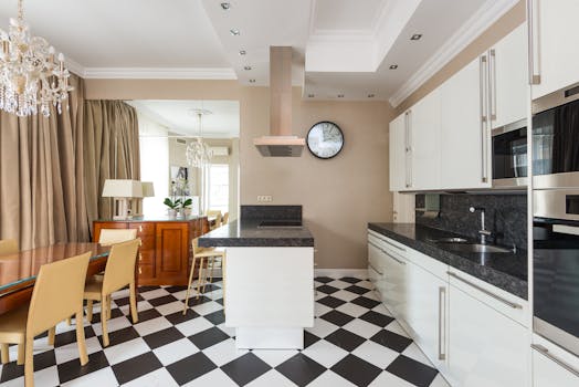 Interior of modern kitchen with marble counter and built in appliances with chairs at wooden dining table in stylish apartment