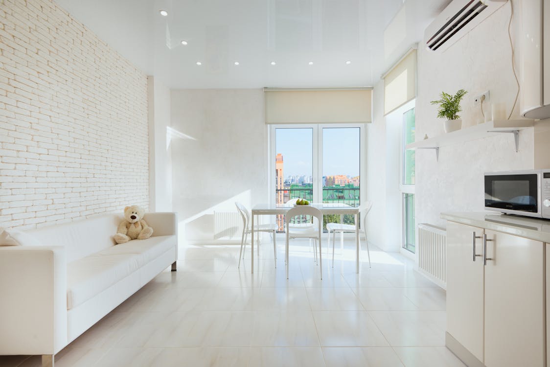 Interior of light kitchen with plush toy on sofa near dining table placed closet to panoramic balcony doors