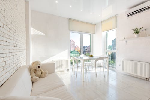 Interior of white kitchen furnished with sofa and chairs and table placed near big windows with blinds