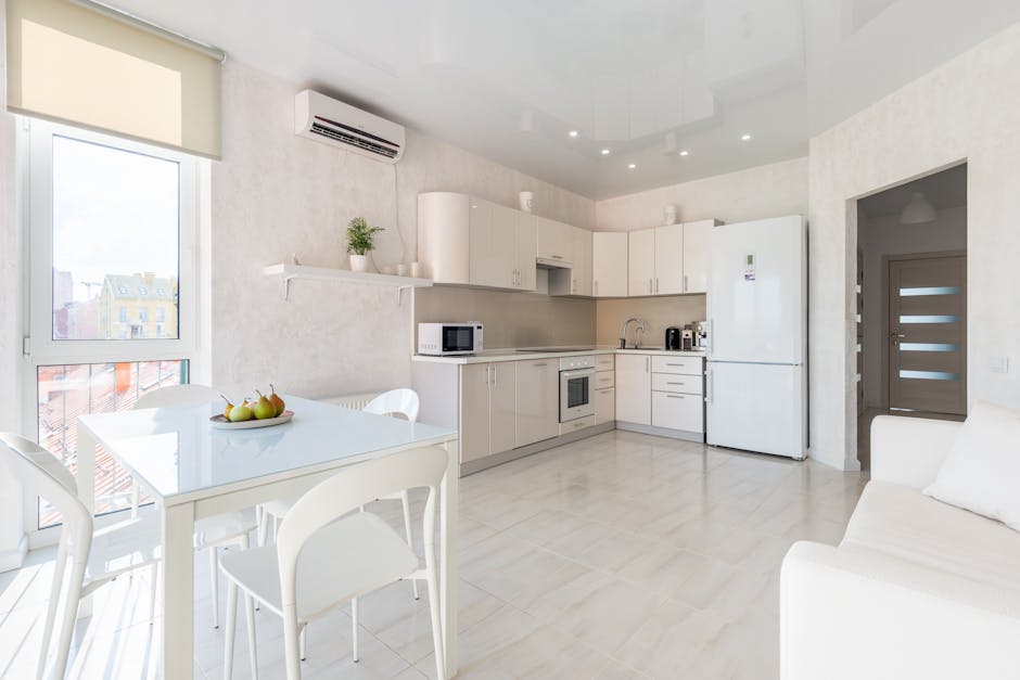 Spacious contemporary kitchen interior featuring white furniture, appliances, and natural light.