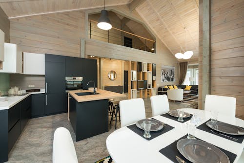 Plates with cutlery and glassware on dining table in stylish kitchen with built in appliances in mansion