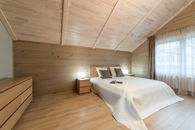 Comfortable bed with pillows and opened magazine with luminous lamps on nightstands on wooden mansard of cottage