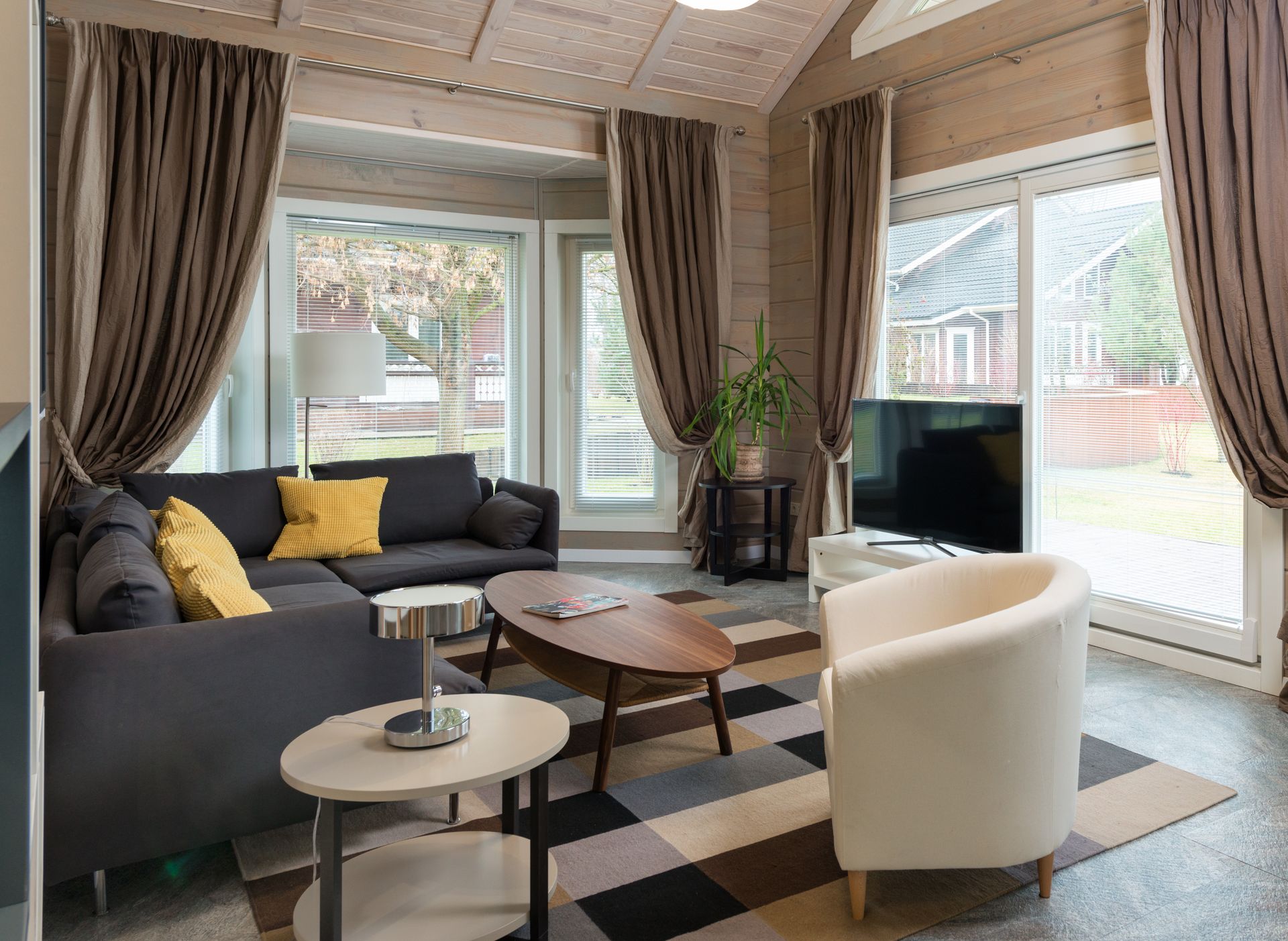 Comfortable corner sofa with cushions placed near round wooden table and armchair in living room equipped with TV set