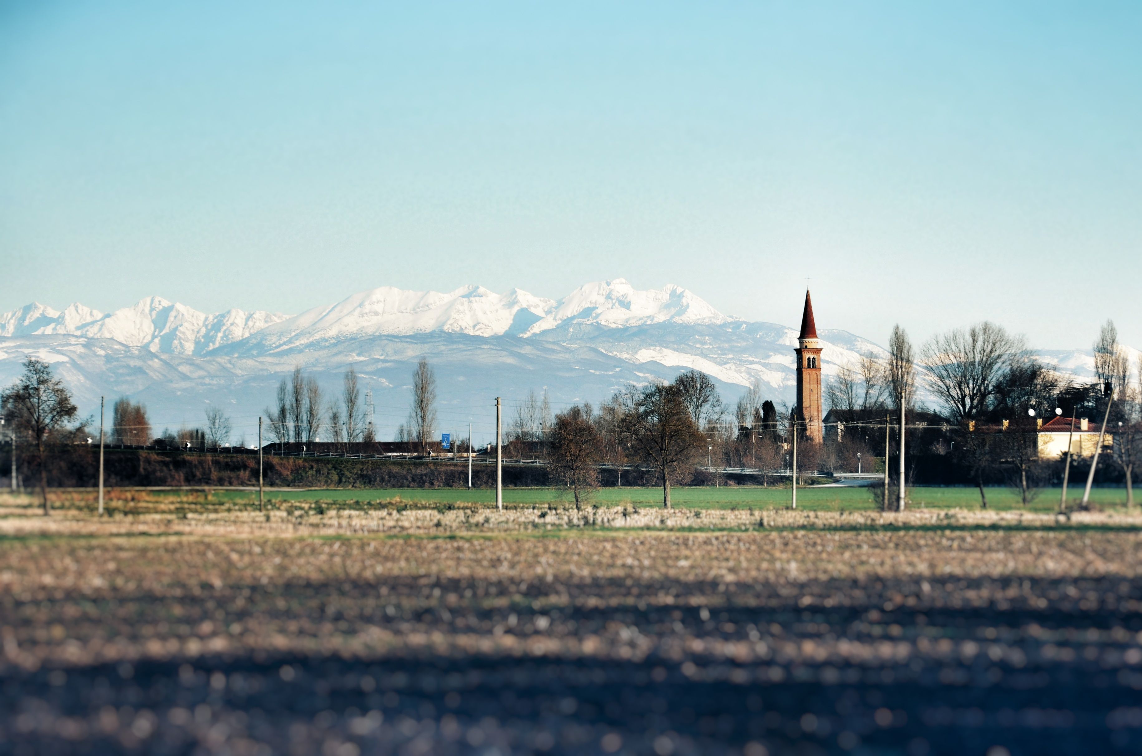 Scenic view of rural landscape with snow-capped mountains and a church tower.