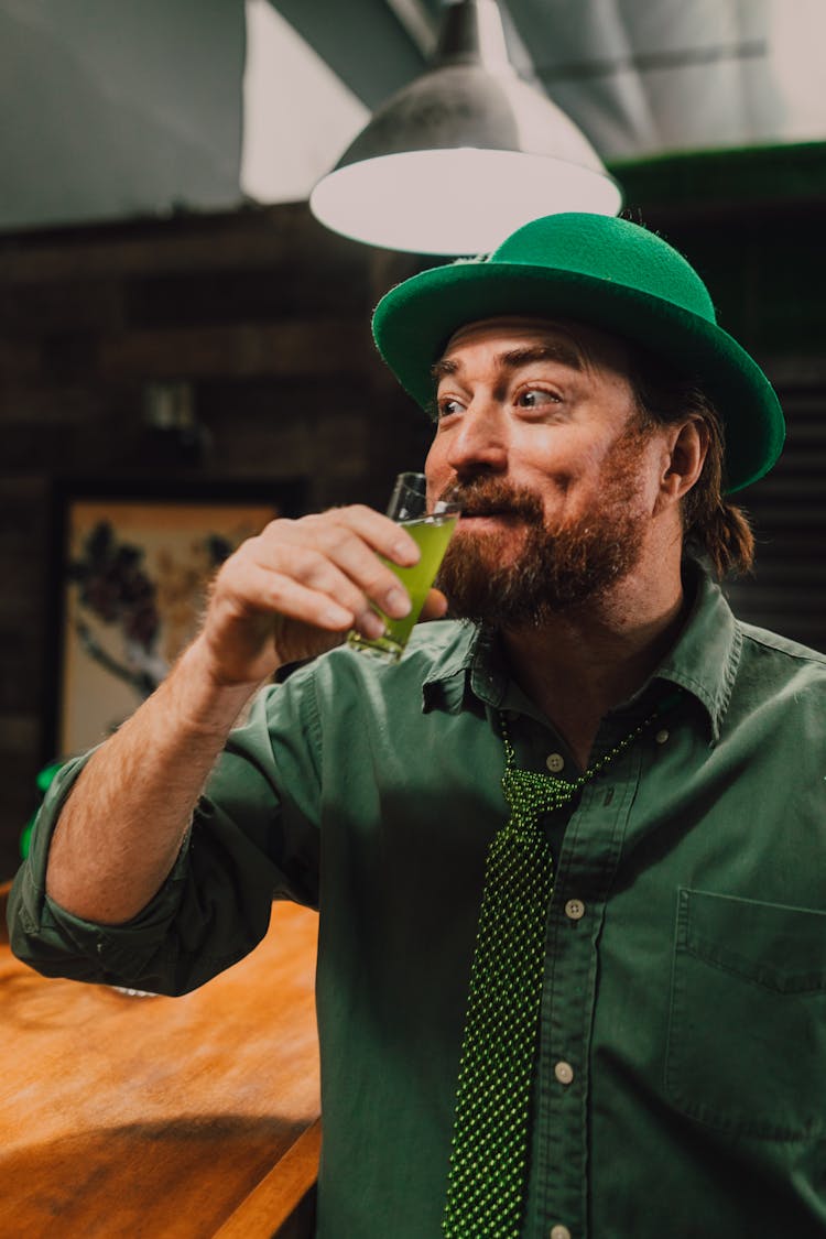 A Man In Green Button Up Shirt And Hat Drinking Green Juice