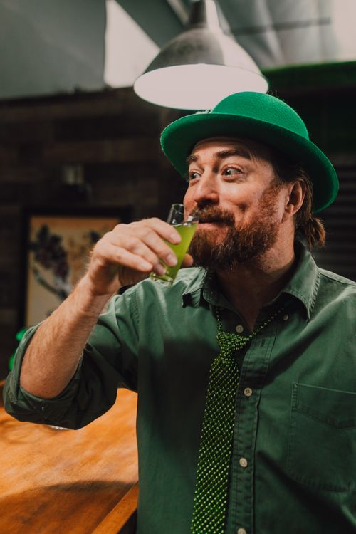 Free Bearded man in green attire enjoying a drink at a St. Patrick's Day party. Stock Photo