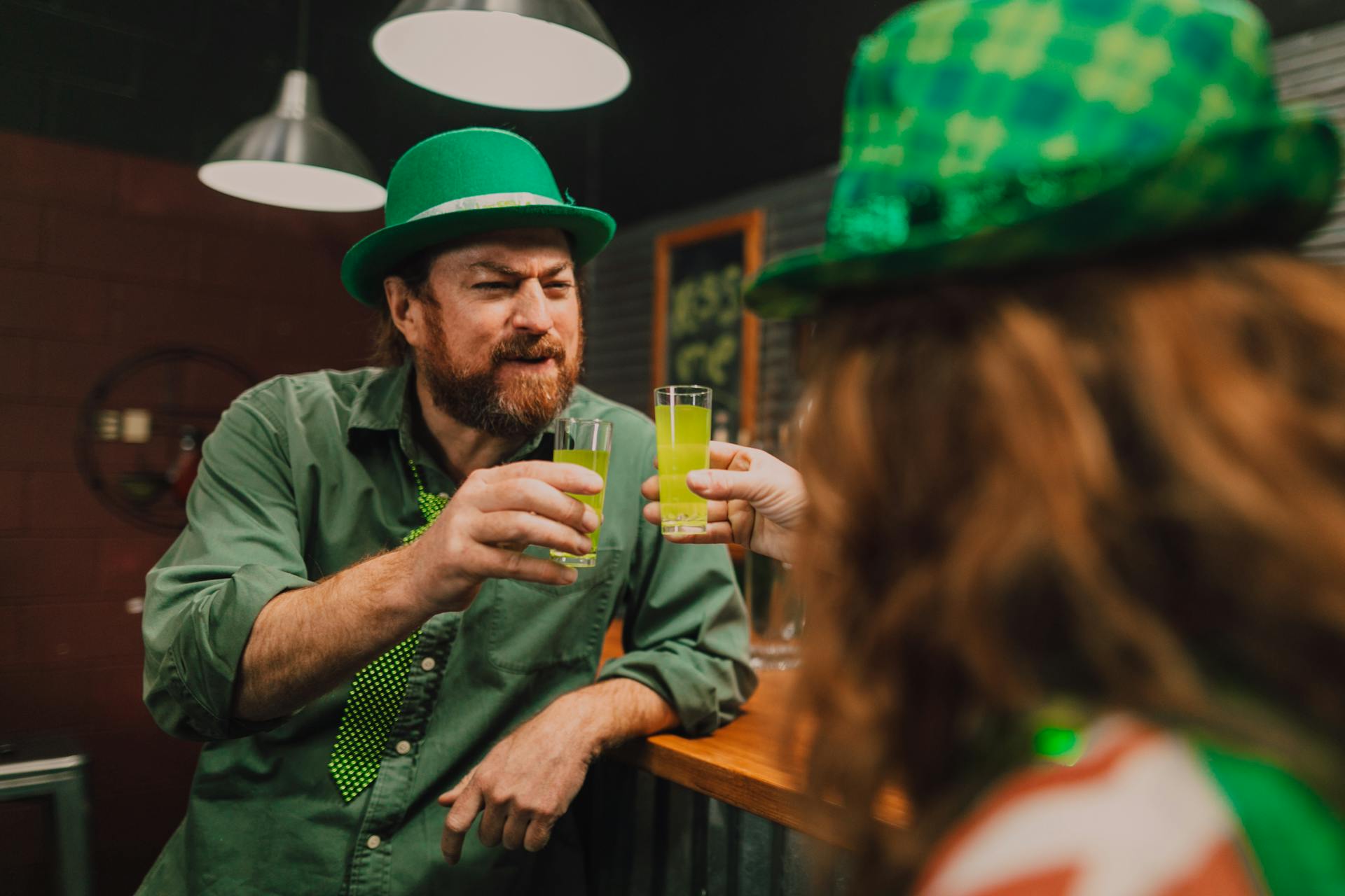 A Man Holding a Shot Glass while Standing in Front of a Person while Leaning on a Bar Counter 