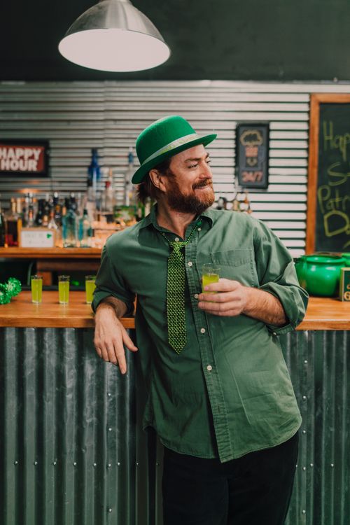 Free Bearded man in green attire celebrating St. Patrick's Day at a festive bar, holding a cocktail. Stock Photo