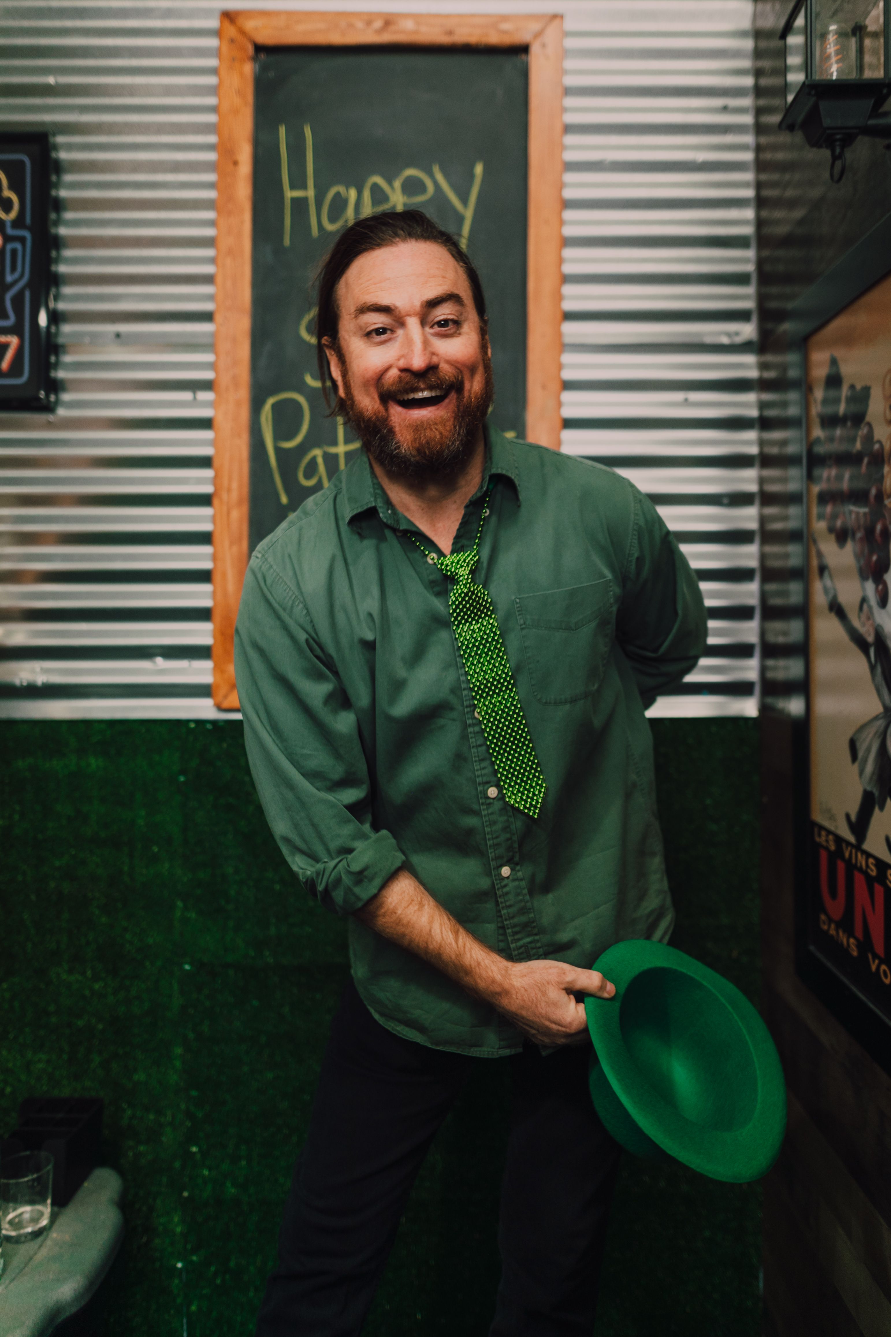 Happy man with green hat and tie celebrating St. Patrick's Day indoors.