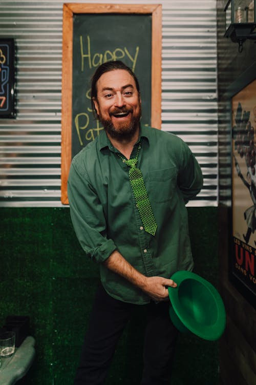 A Happy Man in Green Long Sleeves and Necktie Holding a Hat 