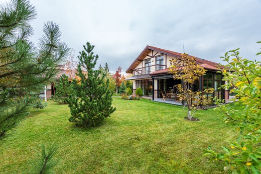 Big private two storey house with terrace surrounded by trees growing on lawn in backyard
