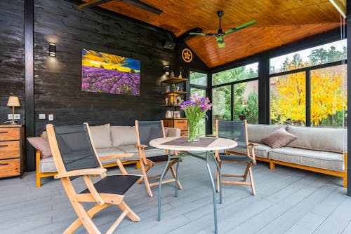 Interior of stylish terrace of villa with armchairs placed near table decorated with vase of flowers and sofas under wooden ceiling