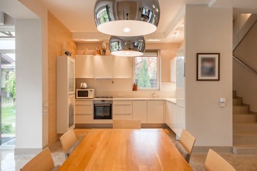 Interior of modern house with wooden table and chairs placed near kitchen with white cabinets and appliances