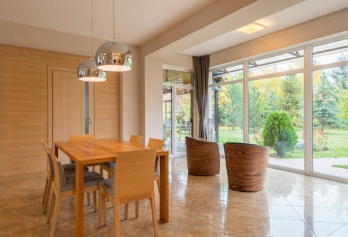 Interior of spacious dining zone with panoramic windows furnished with wooden table and chairs on tilled floor in villa