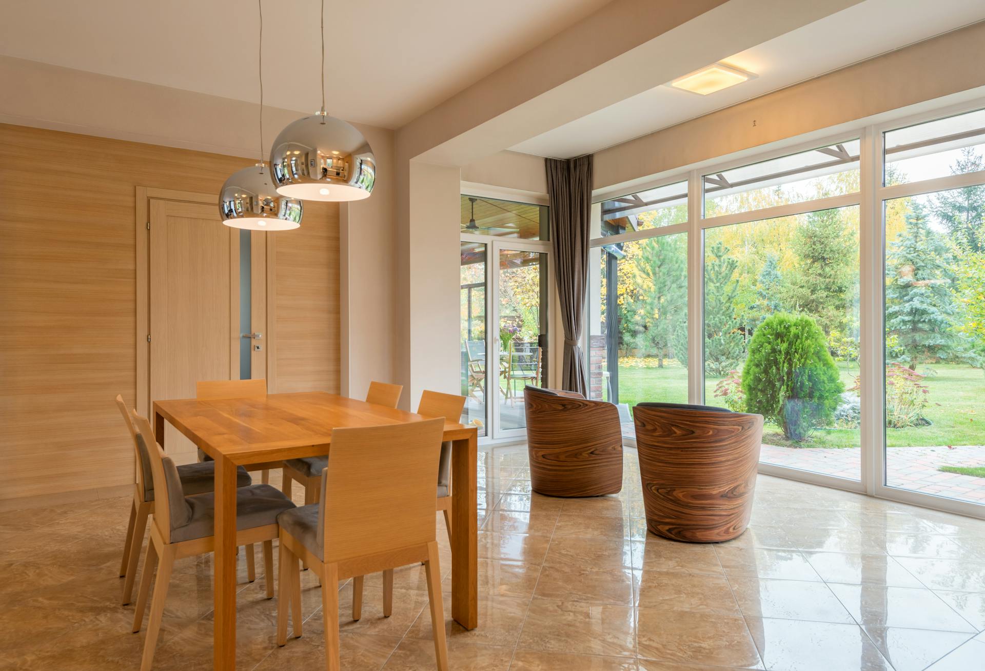 Interior of spacious dining zone with panoramic windows furnished with wooden table and chairs on tilled floor in villa