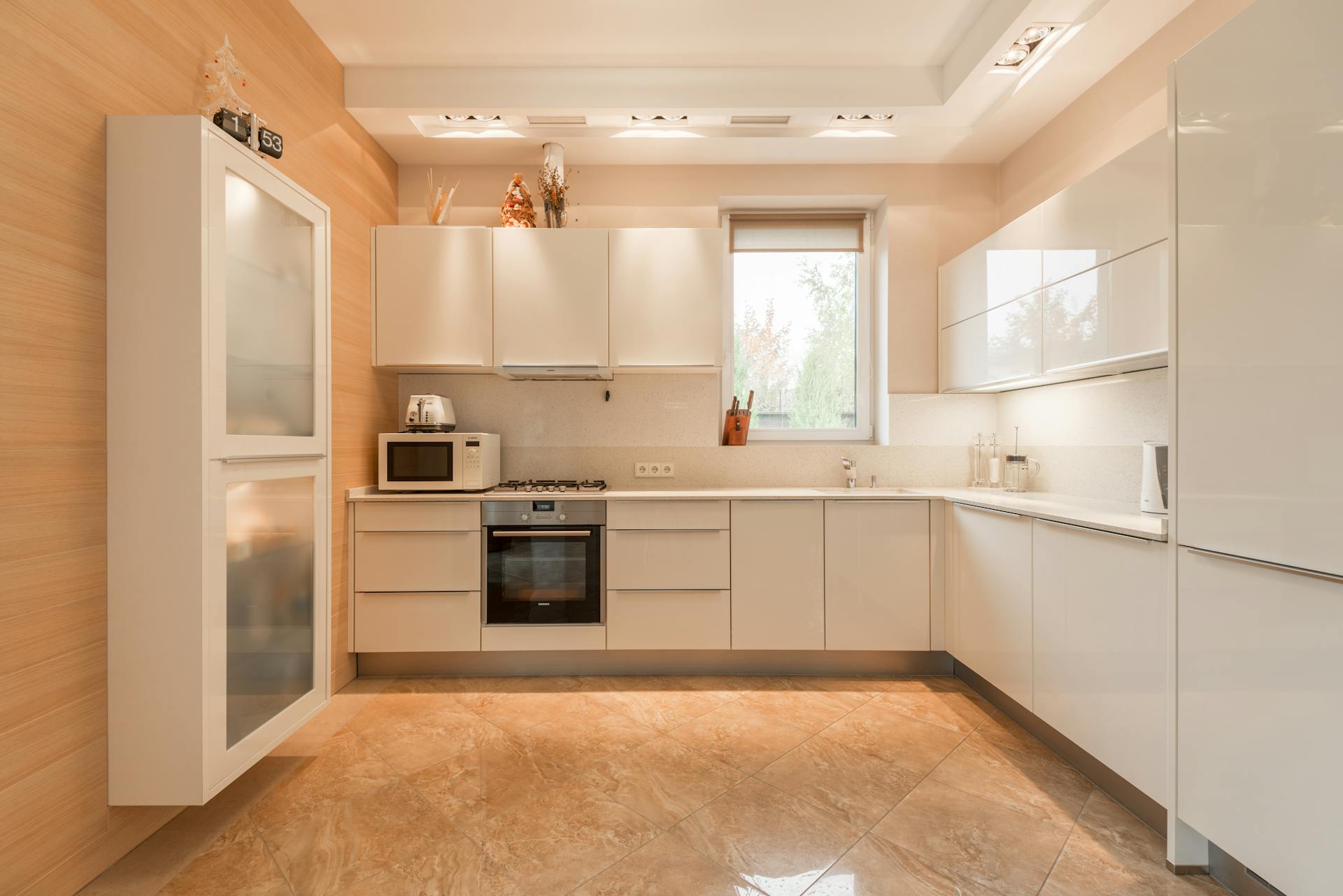 Stylish interior of kitchen with white cupboards and built in oven and stove under lamps on ceiling