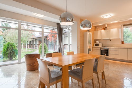 Wooden chairs at table under creative lamps on tiled floor in spacious light kitchen of modern villa
