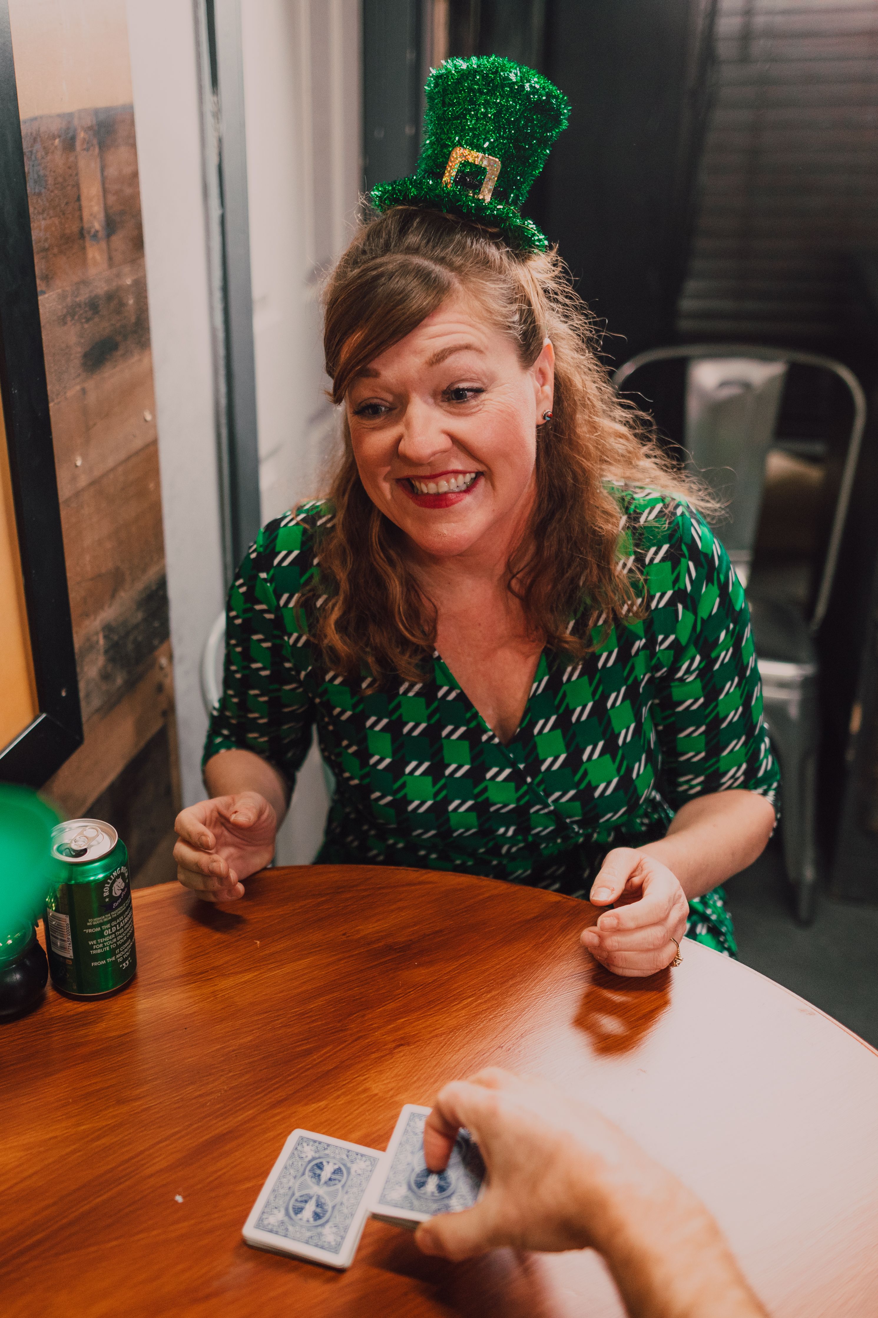 Happy woman in green dress celebrates St Patrick's Day by playing cards indoors.