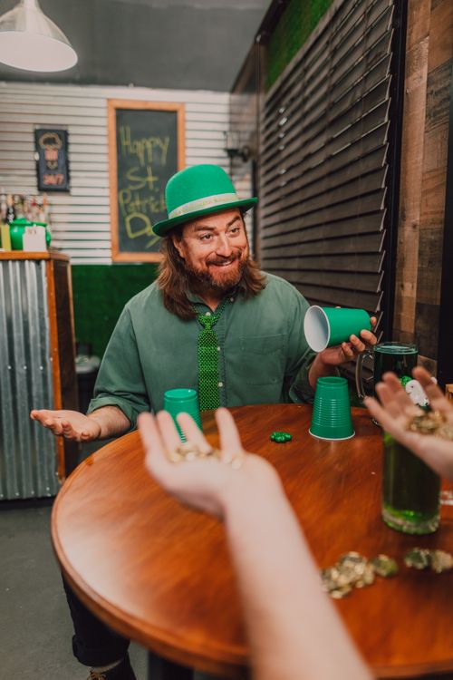Free Man celebrating St. Patrick's Day indoors with drinks and a joyful expression. Stock Photo