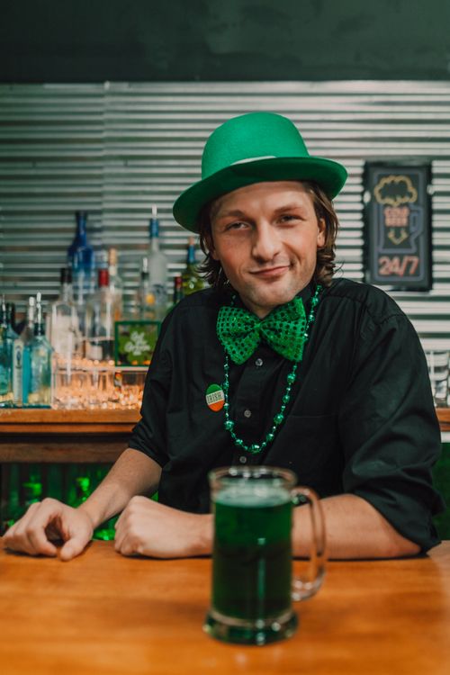 Free Smiling bartender in green attire serves festive drinks for St. Patrick's Day. Stock Photo