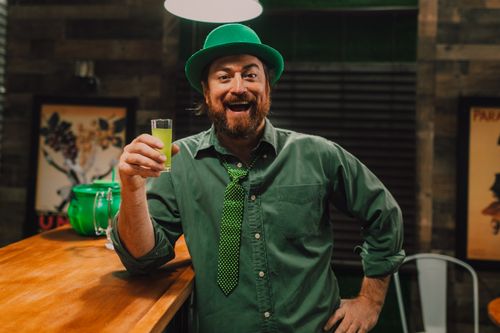 Free Cheerful man in green attire holding a drink, celebrating St. Patrick's Day indoors. Stock Photo