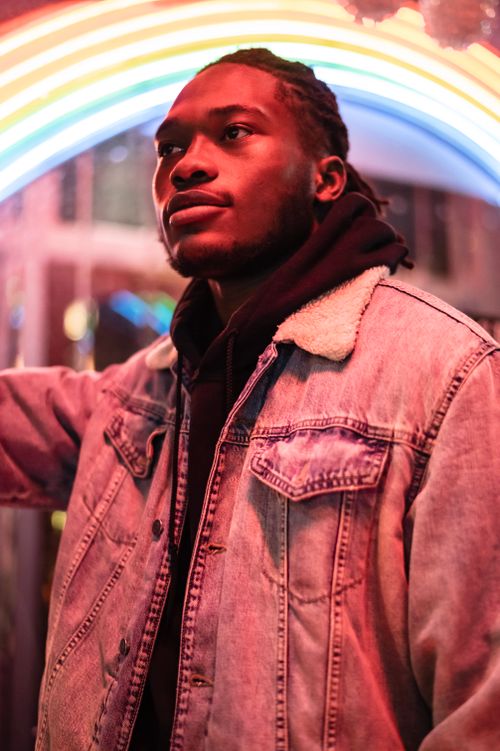 Free Thoughtful African American male in stylish jacket looking away on blurred background of street with luminous lights in late evening Stock Photo