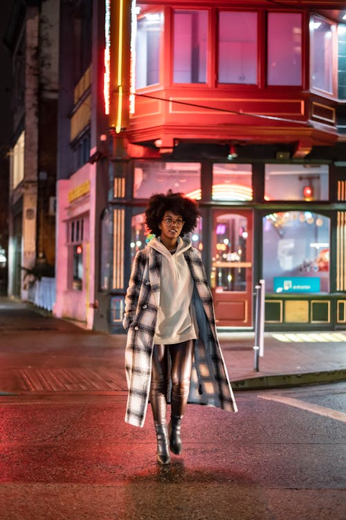 Free Full body of confident African American female wearing trendy outfit walking on crosswalk on city street at night Stock Photo