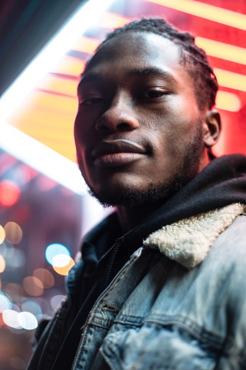 Free Low angle of confident African American male in casual wear against luminous colorful lights looking at camera Stock Photo