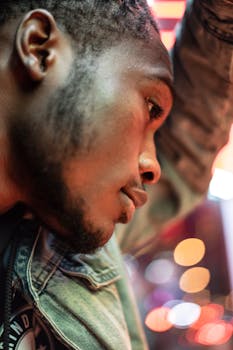 Close-up side profile of a man in denim, illuminated by urban evening lights.
