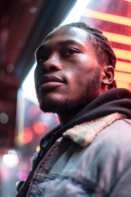 Free Serious bearded African American male with dreadlocks looking away while standing near glass wall of modern building with glowing lights on evening street on blurred background Stock Photo