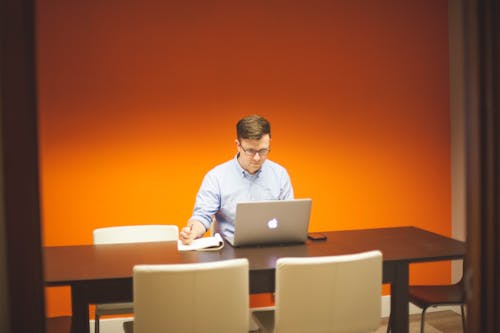 Man Sitting on Chair in Front Table With Silver Macbook