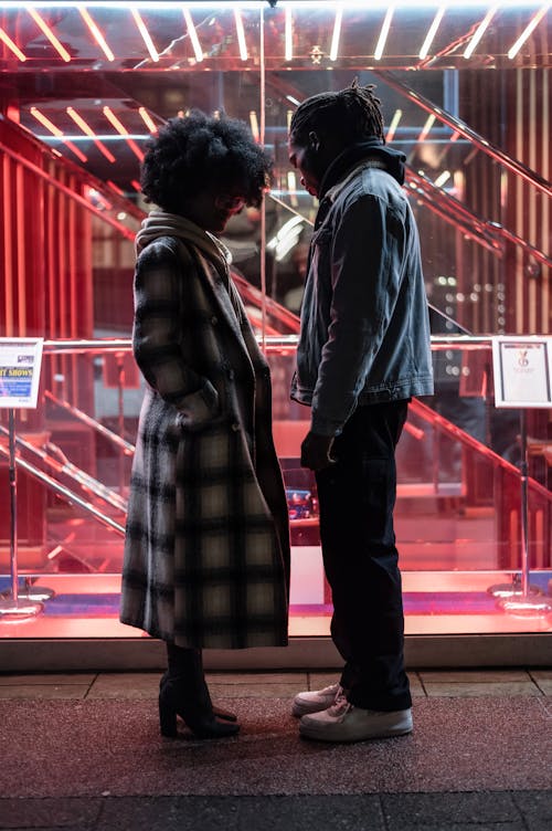 Free Side view full body of unhappy African American couple standing on street near glass wall with glowing lights Stock Photo