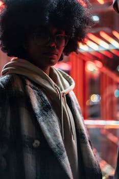 Portrait of a young woman with afro hair in stylish coat, illuminated by neon lights.