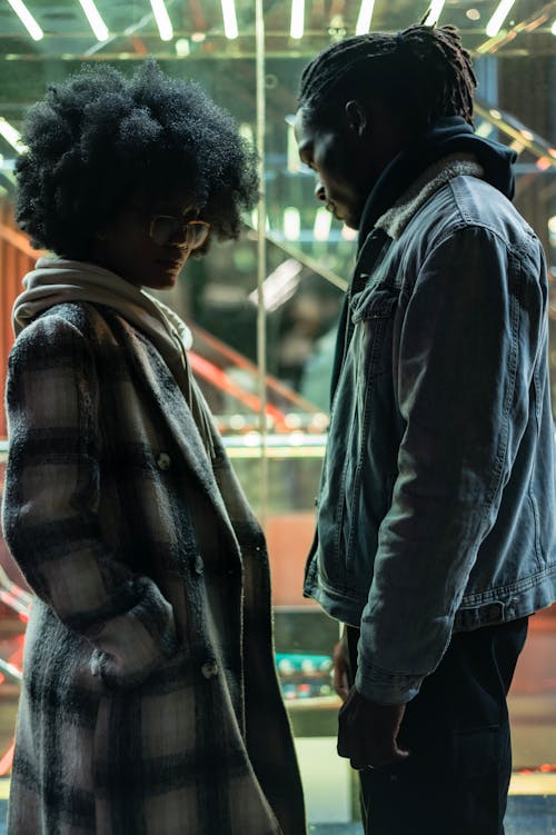 Free Side view of displease African American couple having misunderstanding and difficulties in relationship standing near glass wall at night Stock Photo