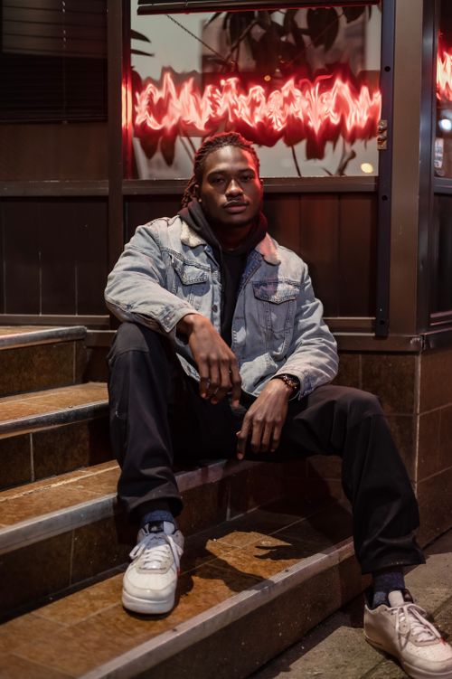 Free Full body of confident African American male wearing denim jacket looking at camera while sitting on steps on street in evening time Stock Photo