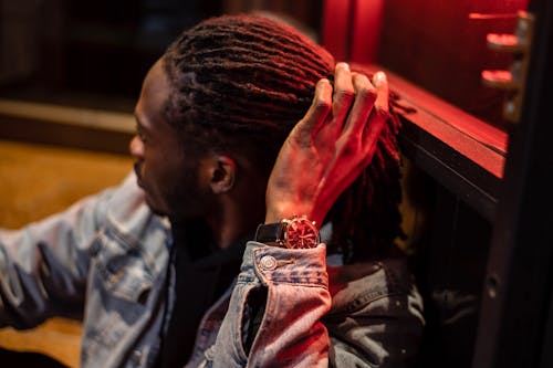 Black man in wristwatch adjusting dreadlocks near building