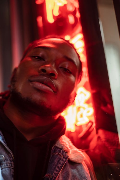 Low angle of serious bearded African American male against glowing red signboard at night