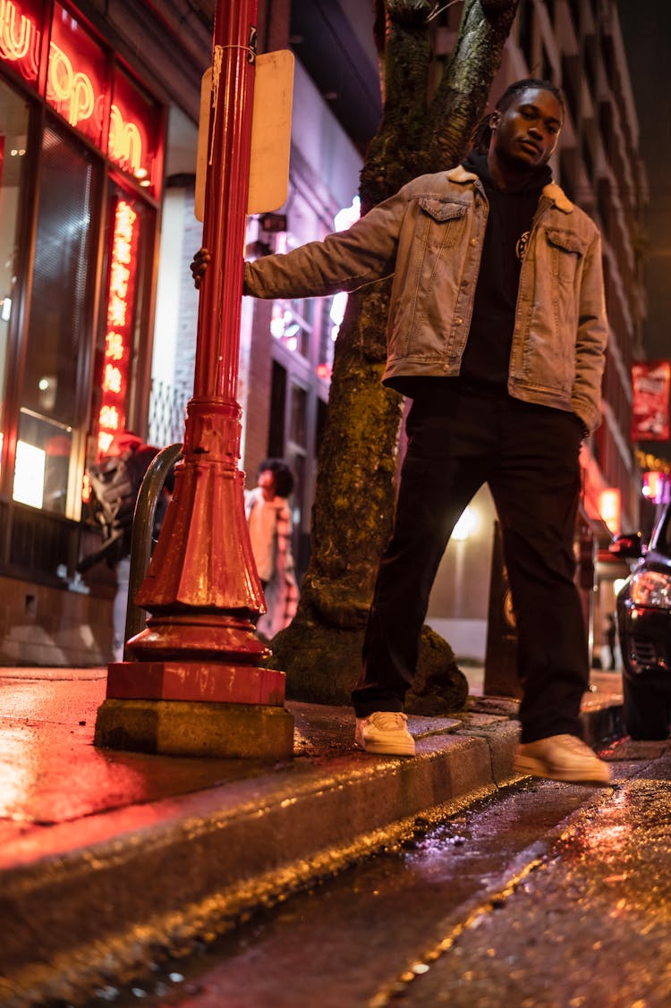 Serious Black Man Holding Post On Sidewalk At Night