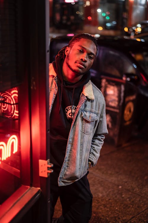Free Confident African American male in casual clothes standing with hand in pocket near glowing red neon and looking at camera Stock Photo