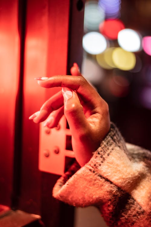 Hand of unrecognizable female in stylish outerwear touching wooden frame of building while standing on street in evening time on blurred background