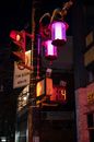 Lanterns on post with restriction sign and numbers with letters against city building at dusk