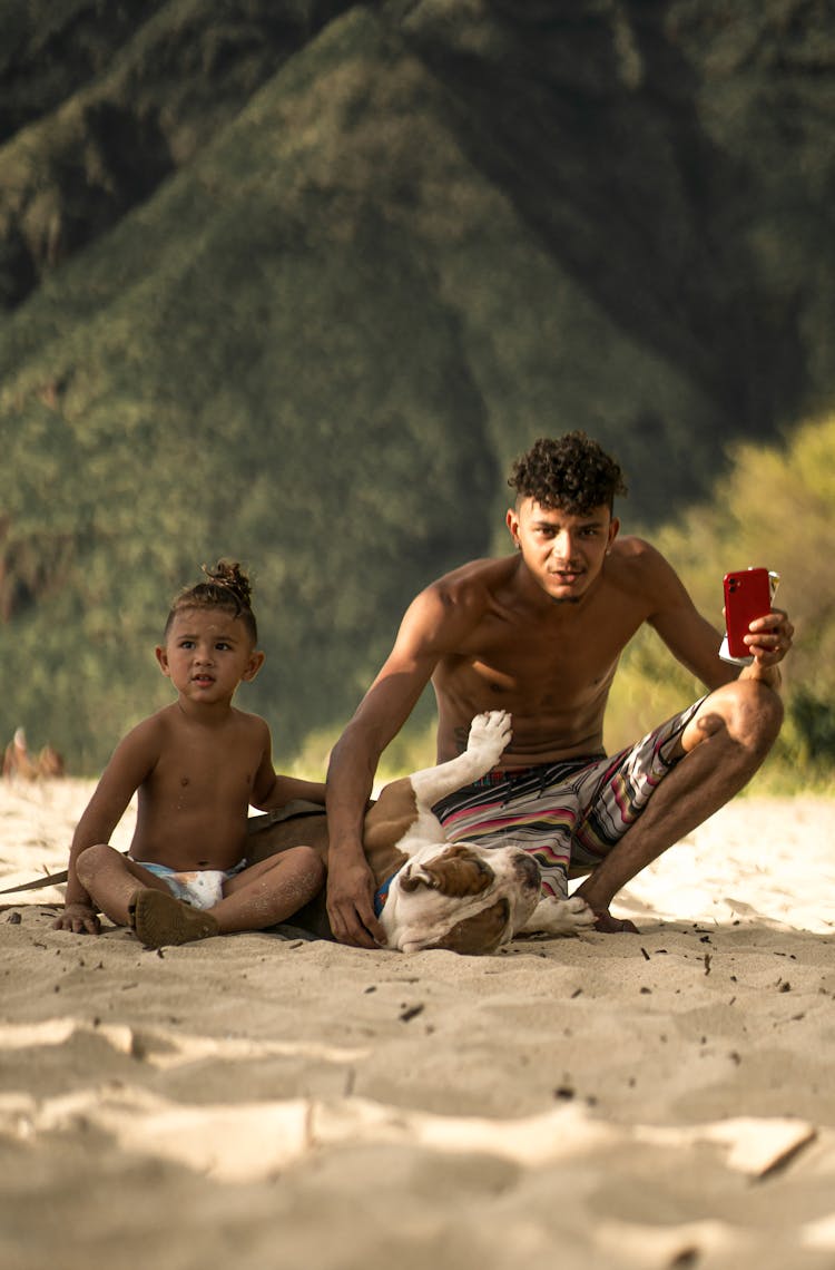 Hispanic Man Playing With Dog Near Child On Sandy Beach