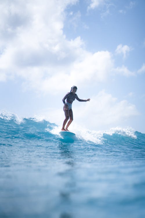 Full length of lady surfing on surfboard in wavy ocean in daylight under blue cloudy sky
