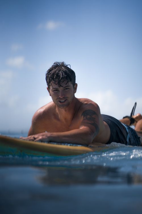 Free Positive shirtless male surfer lying on surfboard in sea while looking at camera under blue cloudy sky in sunny day Stock Photo