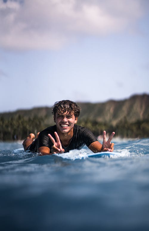 Smiling male showing V sign lying on surfboard
