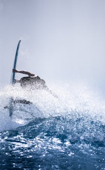 Anonymous strong surfer holding surfboard while flipping over wave in sparkling splashes in sunlight