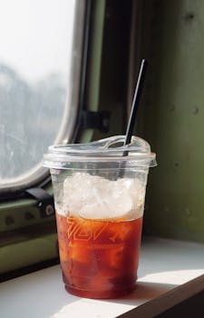 Close-up of iced coffee in a plastic cup by a window. Perfect for summer refreshment.
