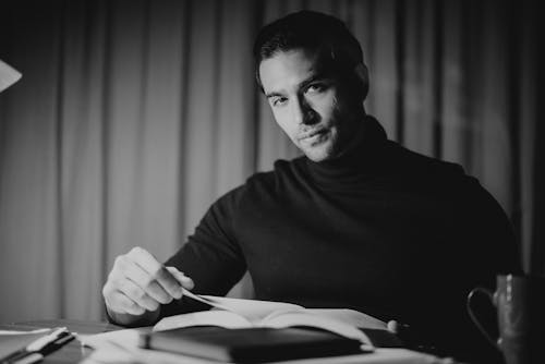 Young calm man reading book in home office