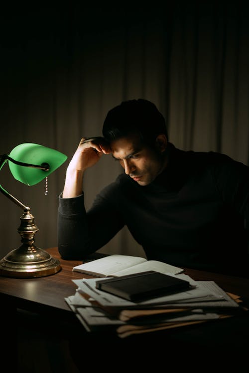 Serious man reading book in dark home office