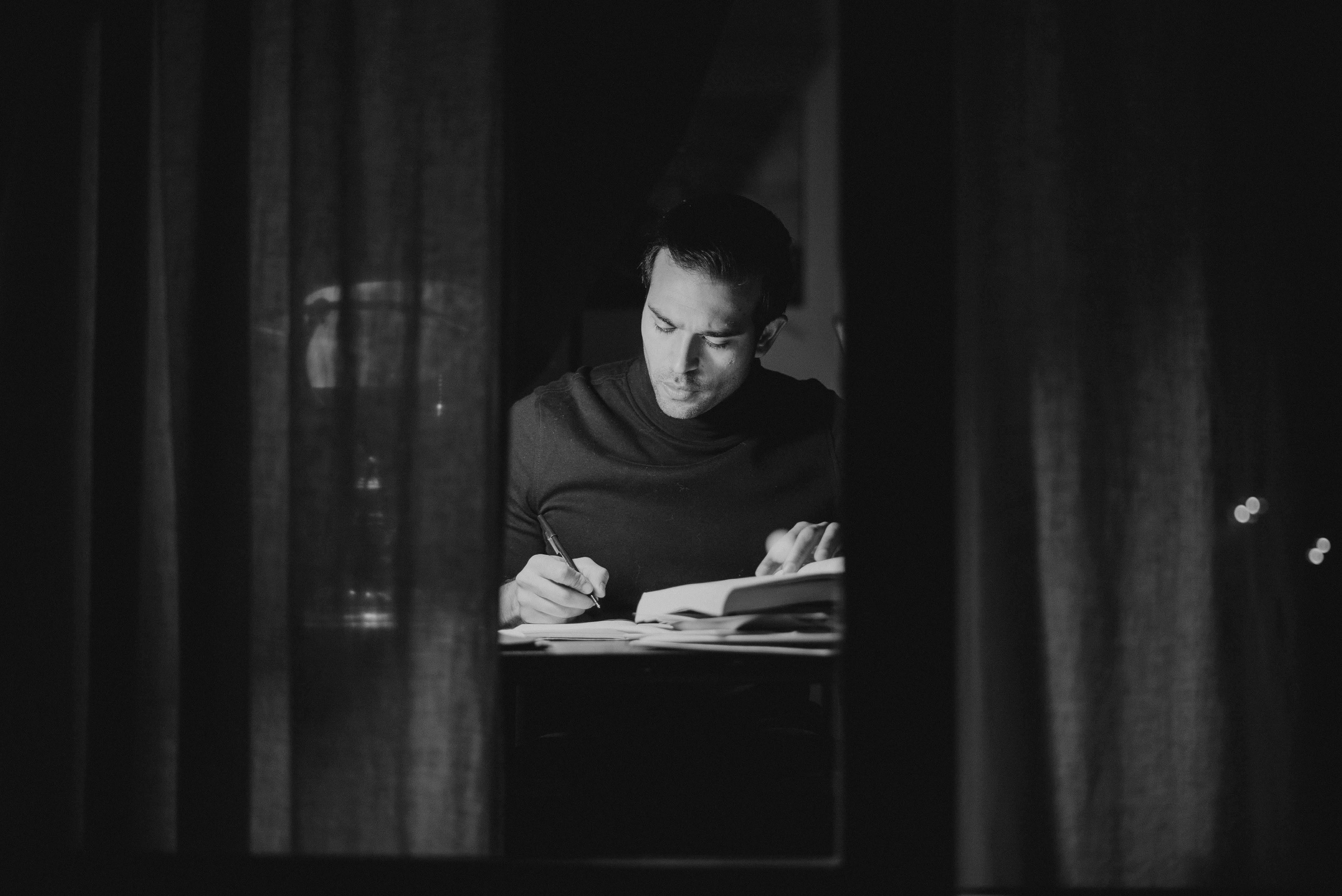 pensive man writing in notebook and reading book